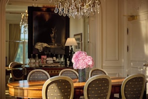 A dining area with a round table, chairs, a vase with flowers, a chandelier, and a large painting on the wall. - InterContinental Amstel Amsterdam by IHG (Amsterdam)