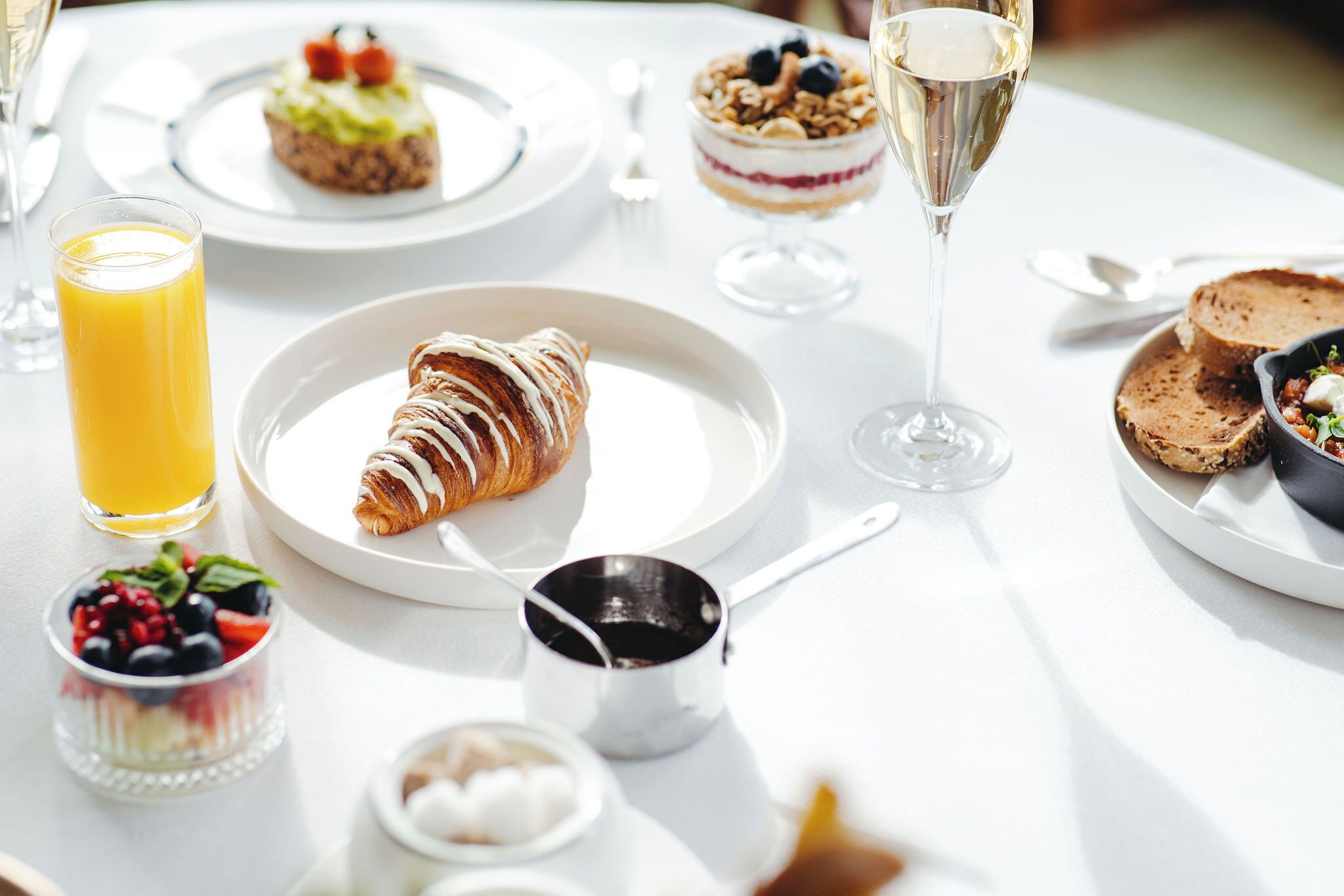 A breakfast setting with croissants, fruit, and a glass of orange juice on a white table.