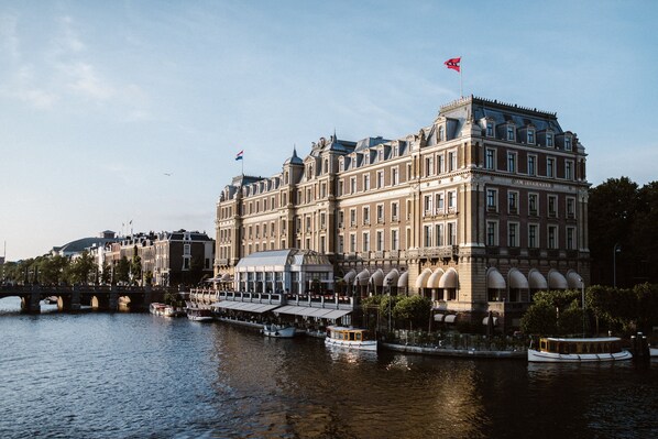 Un edificio grande e histórico con una enseña destacada, ubicado junto a un río con barcos.