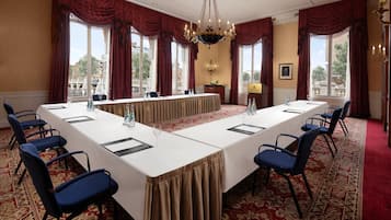 A conference room with a long table, blue chairs, red curtains, and a chandelier.