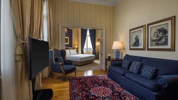 Quarto de hotel com cama, sofá azul, tapete estampado, televisão e duas quadros na parede.