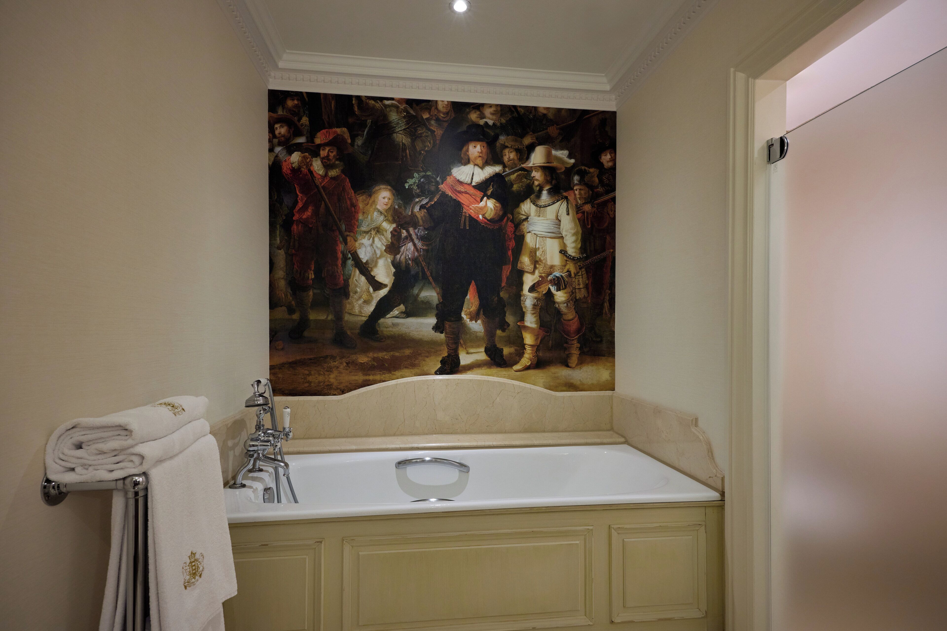 A bathroom with a large classical painting on the wall, a white bathtub, and a towel rack with neatly folded towels.