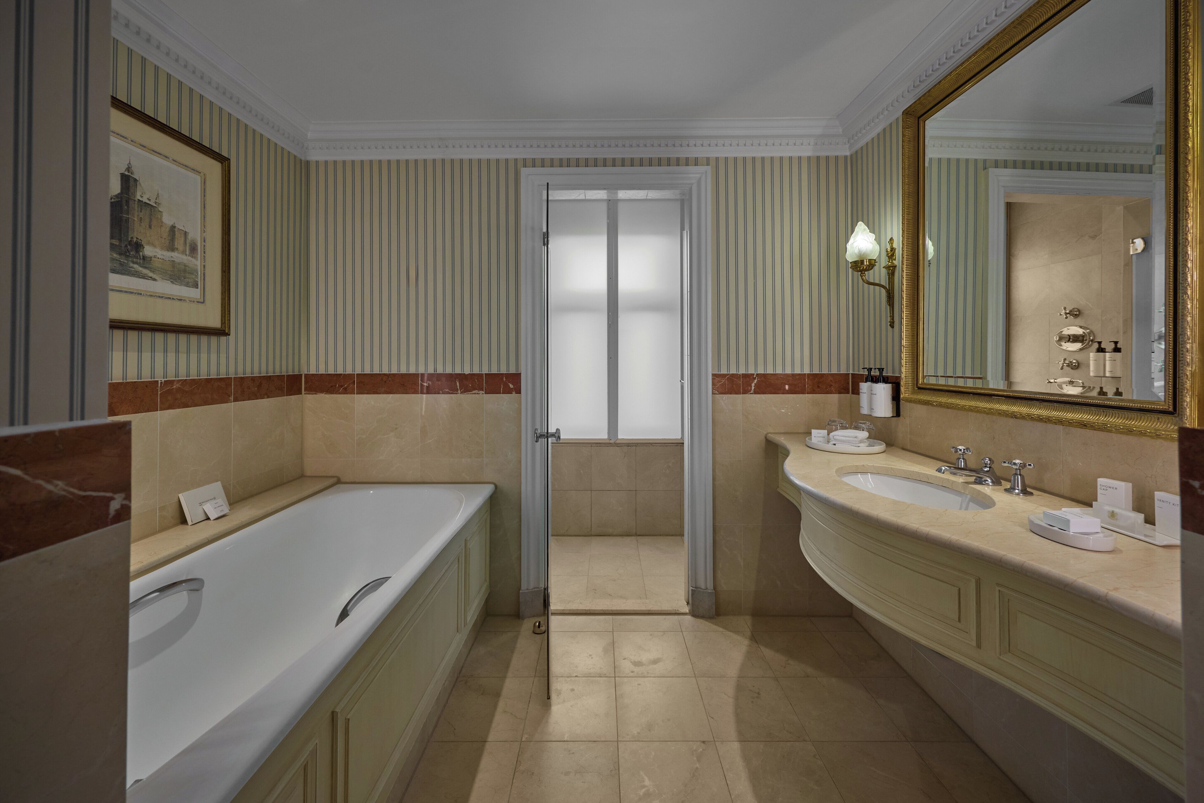 A hotel bathroom with a large bathtub, two sinks, a mirror, and a framed picture on the wall.