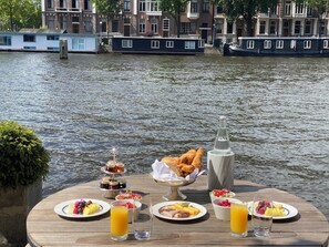 A table set with breakfast items and a view of a canal with boats.
