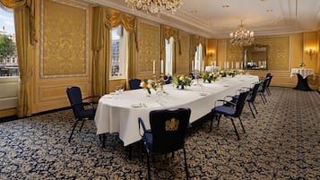 A long dining table set with white tablecloths, candles, and floral centerpieces in a room with patterned carpet and gold accents.