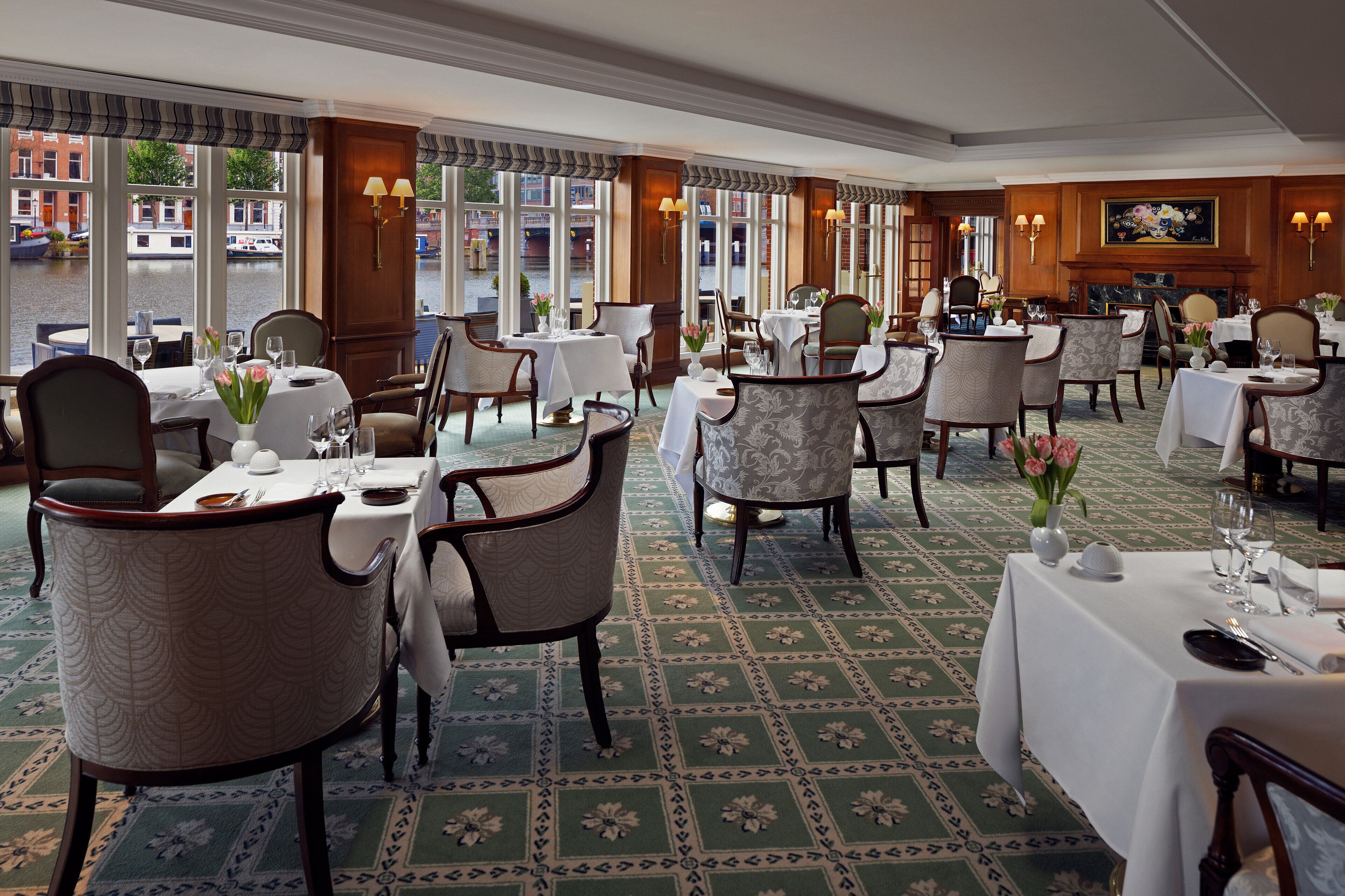 A restaurant with multiple tables and chairs, large windows with a view of the street, and a patterned floor.