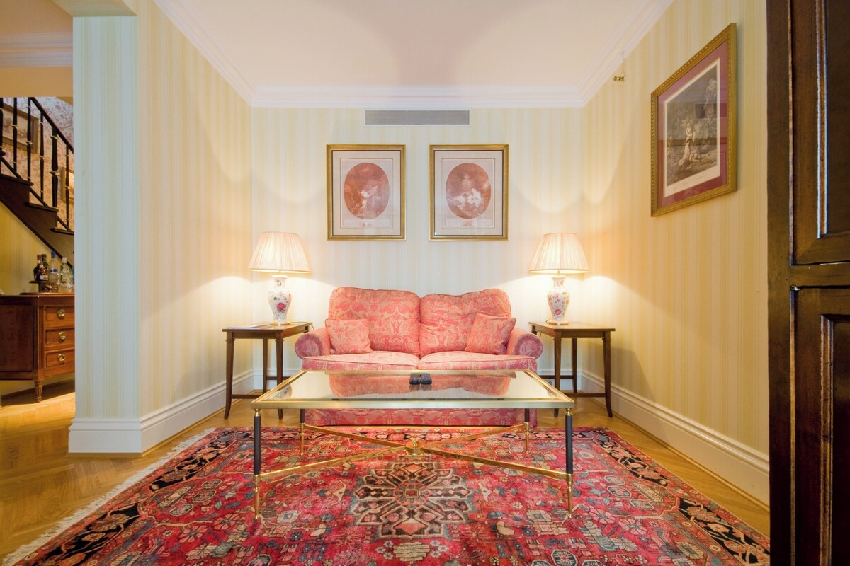 A living room with a pink sofa, two lamps, a glass coffee table, and a patterned rug.