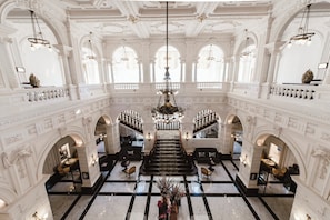 A grand interior with a central staircase, ornate columns, and a chandelier.