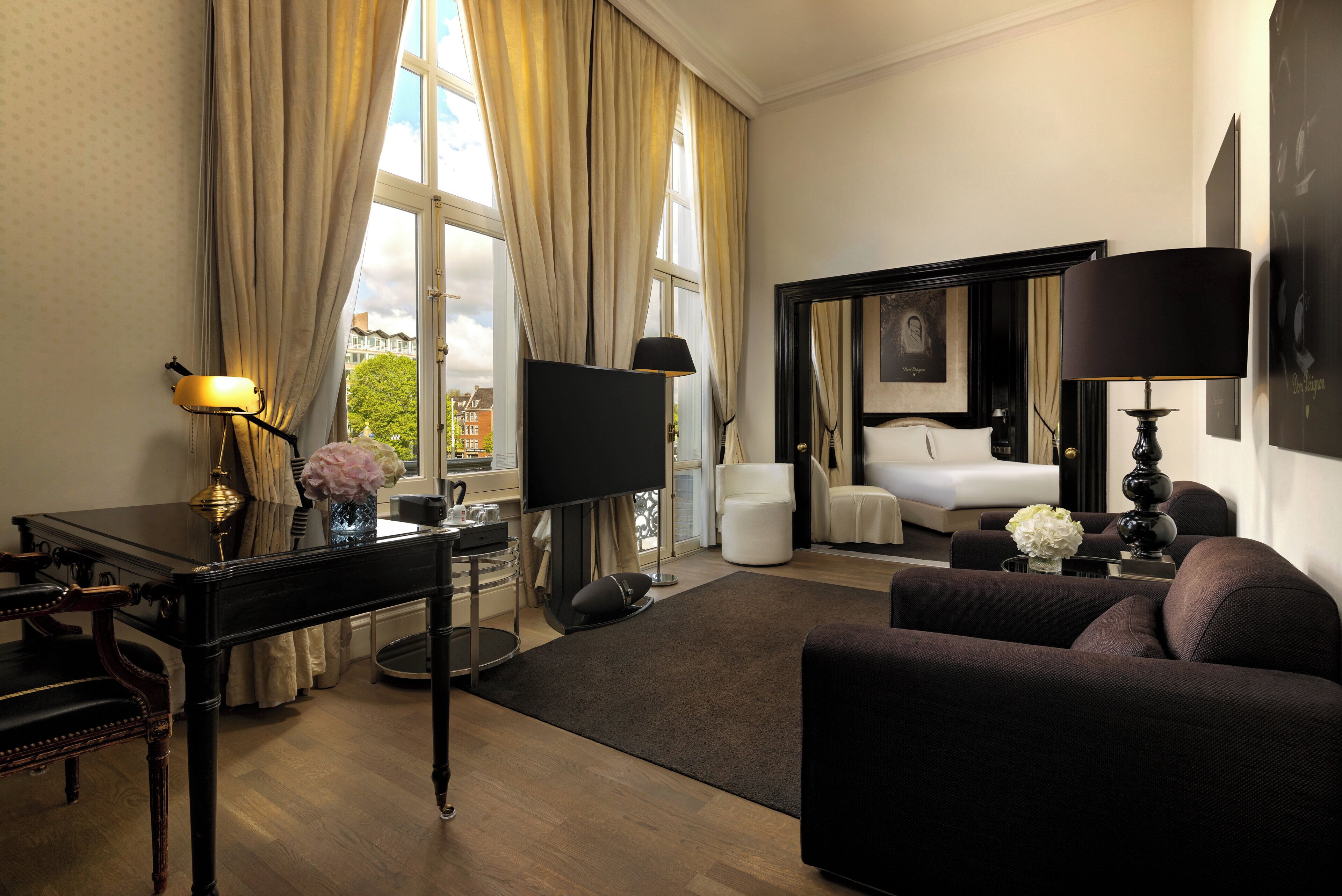 A hotel room with a bed, a sitting area with a sofa, a desk with a lamp, and a TV.