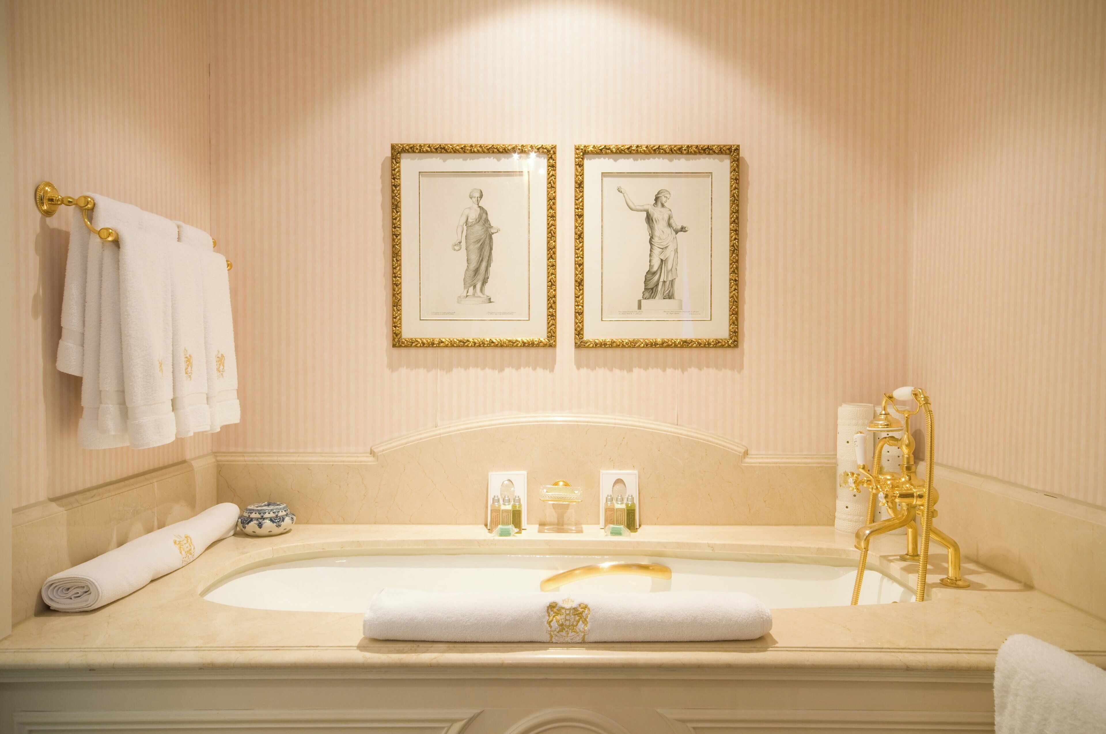 A luxurious bathroom with a large bathtub, gold fixtures, and two framed artworks on the wall.