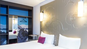 A modern hotel room with a large bed, a nightstand, a wall-mounted light, and a view of mountains. - VISIONAPARTMENTS Geneva Gare  (Geneva)