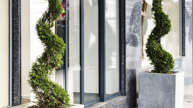 A modern building facade with a logo, large glass windows, and two potted topiary plants. - VISIONAPARTMENTS Geneva Gare  (Geneva)