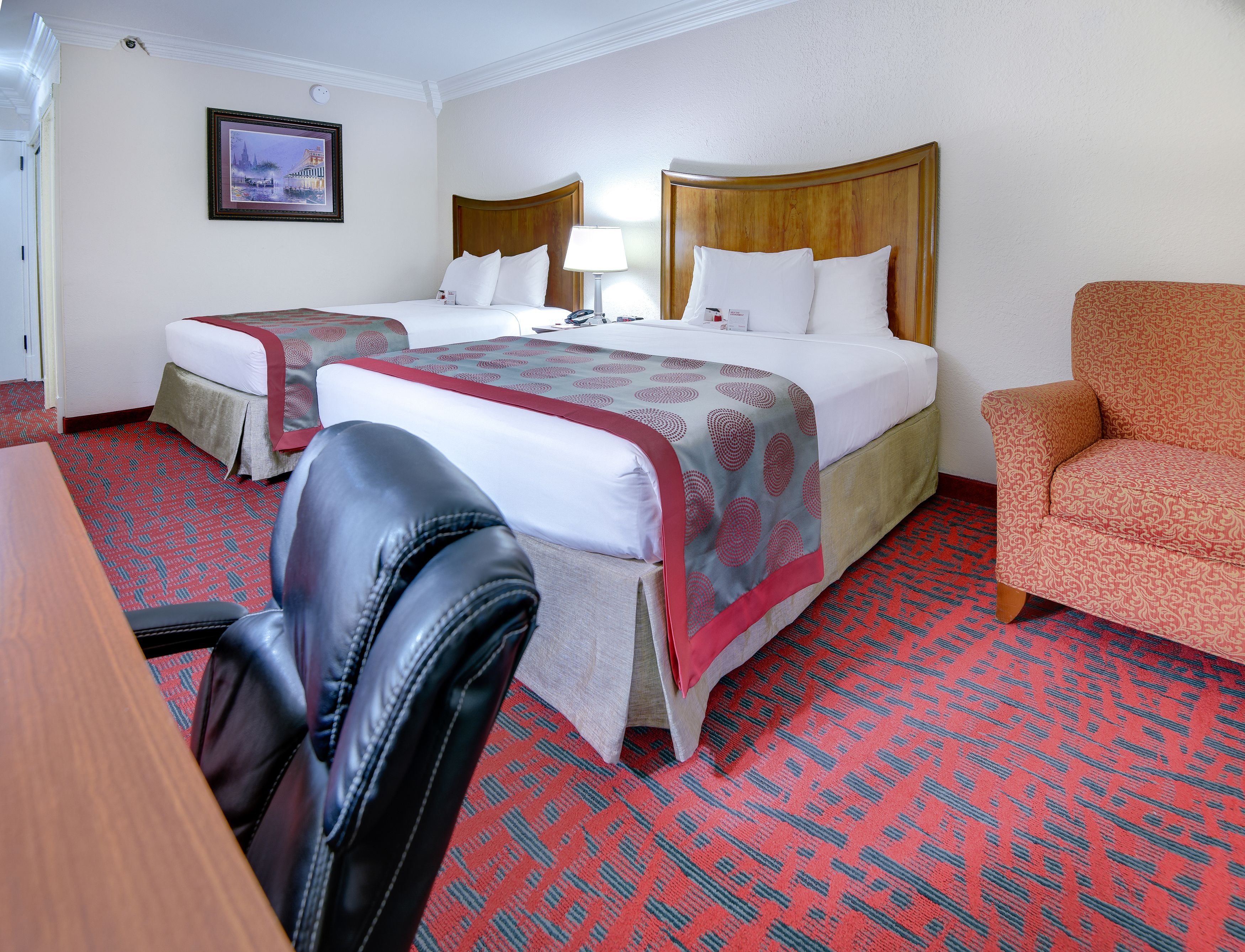 Ein Hotelzimmer mit zwei Betten, einem Schreibtisch, einem Stuhl und einem gemusterten Teppich.