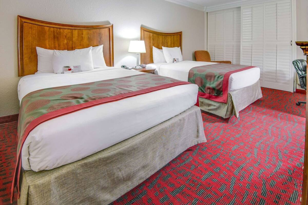 Ein Hotelzimmer mit zwei Betten, einem roten Teppich mit Muster und einem Holzkopfende.
