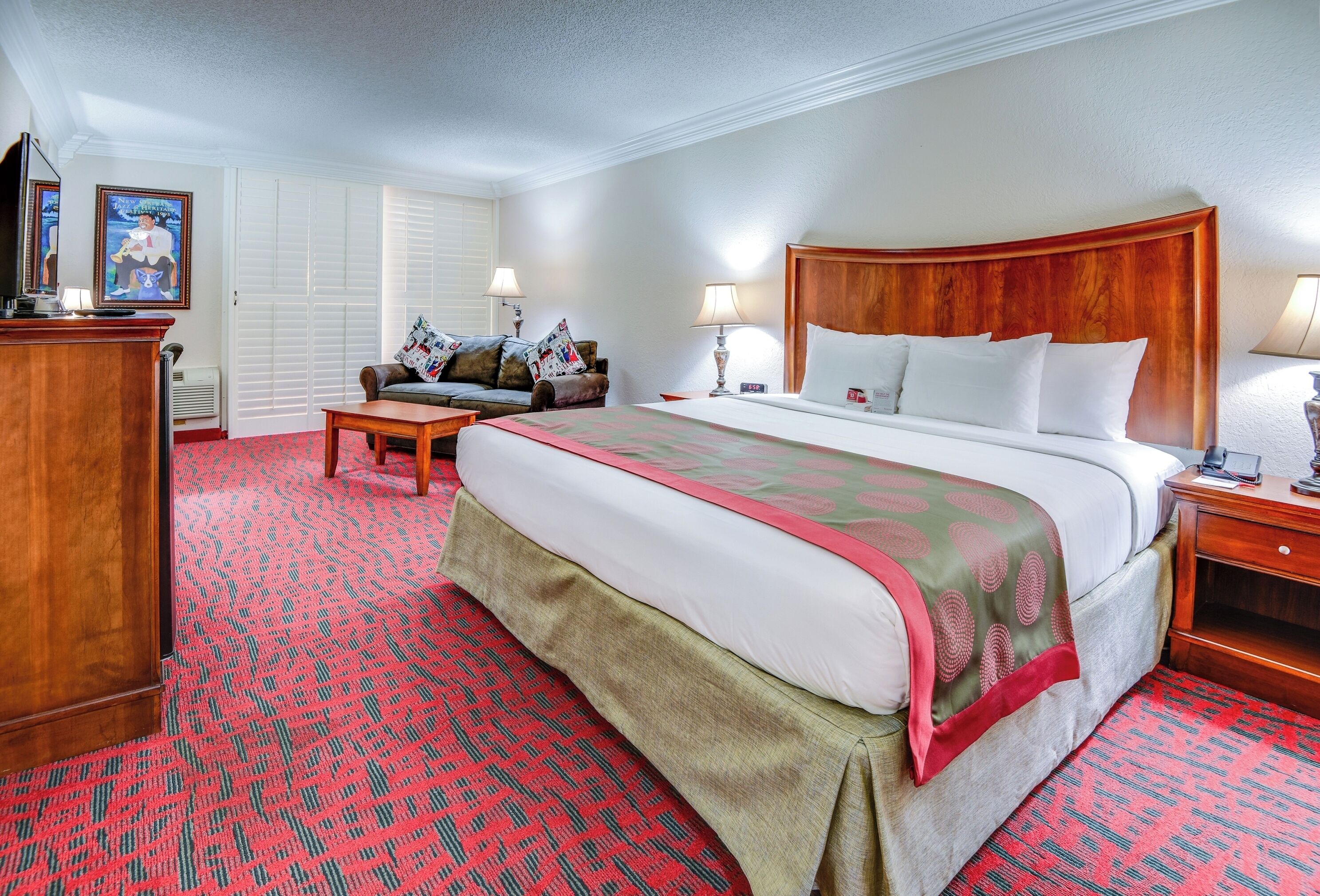Una habitación de hotel con una cama, un escritorio, una silla, un aparador y una ventana con persianas.