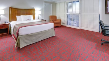 A hotel room with a large bed, a chair, a desk, and a window with blinds.