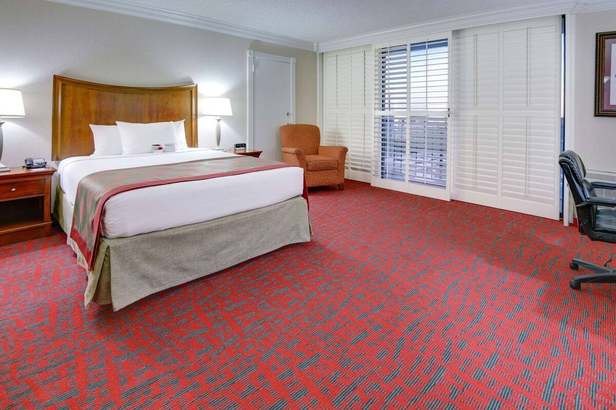 Ein Hotelzimmer mit Bett, Stuhl, Schreibtisch und einem Fenster mit Jalousien.