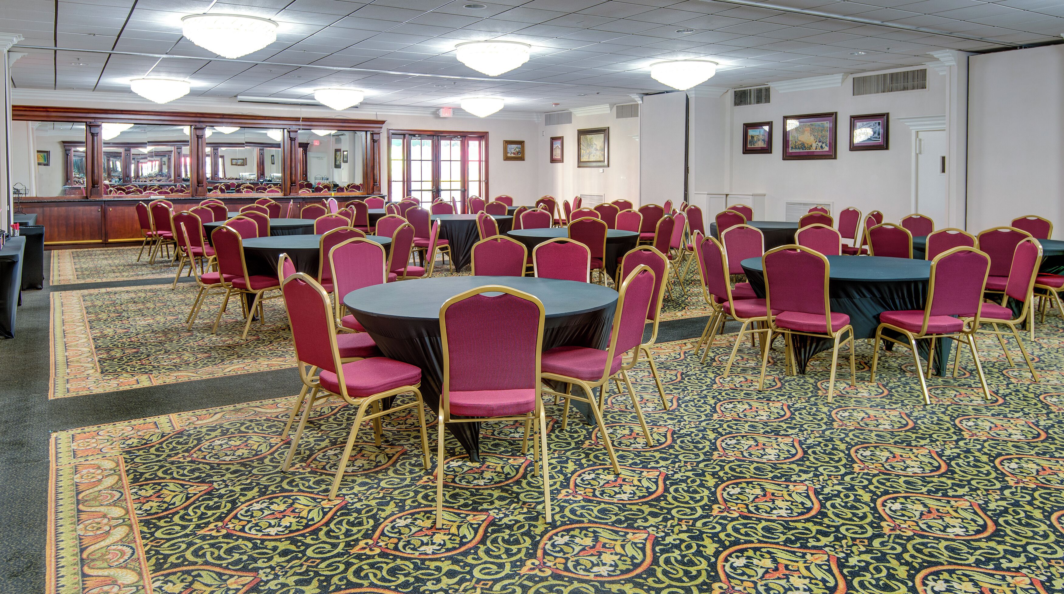 Une salle de conférence dotée de plusieurs tables et chaises, d’un sol recouvert de moquette et de lustres.