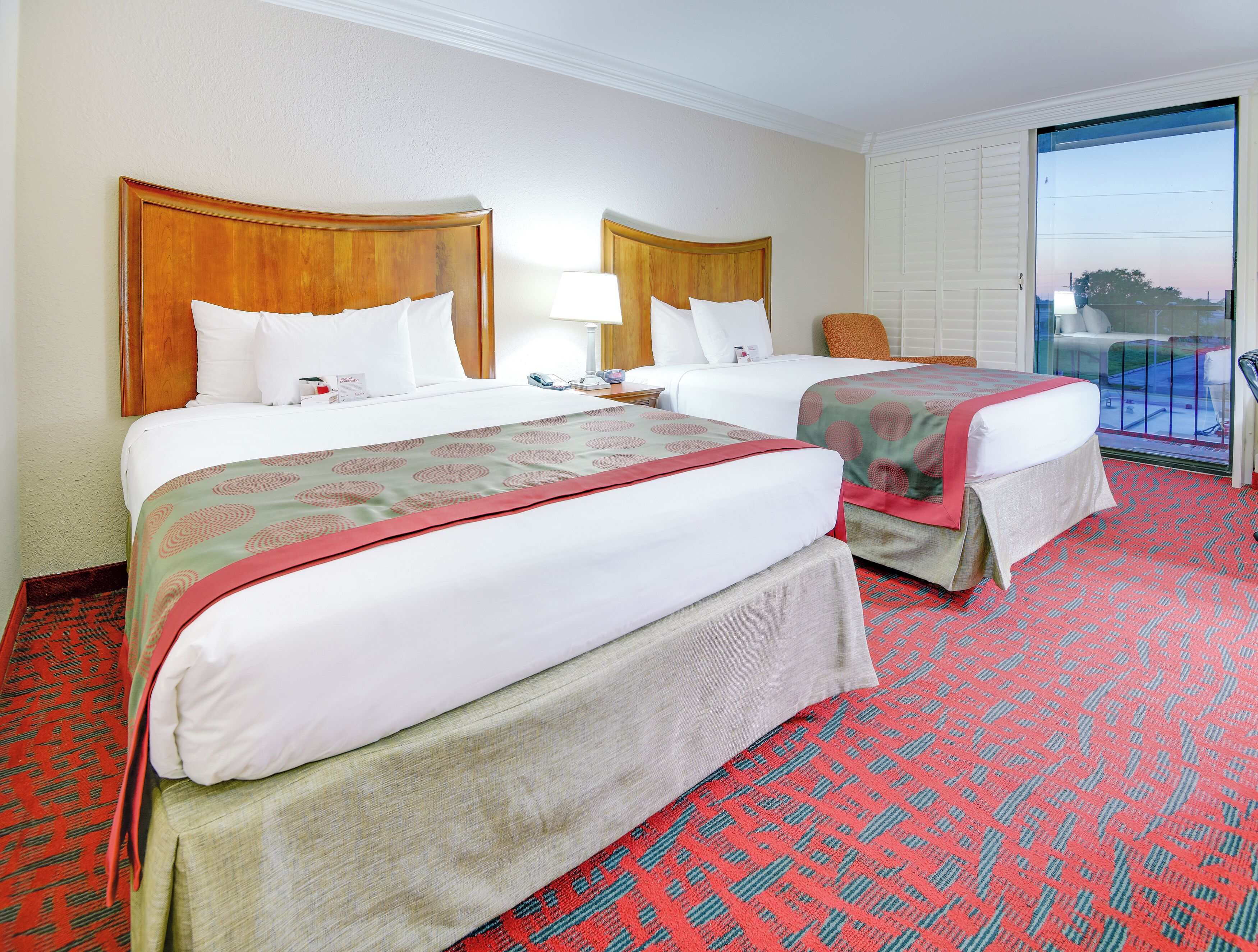 A hotel room with two beds, a balcony, and a view of the outside.