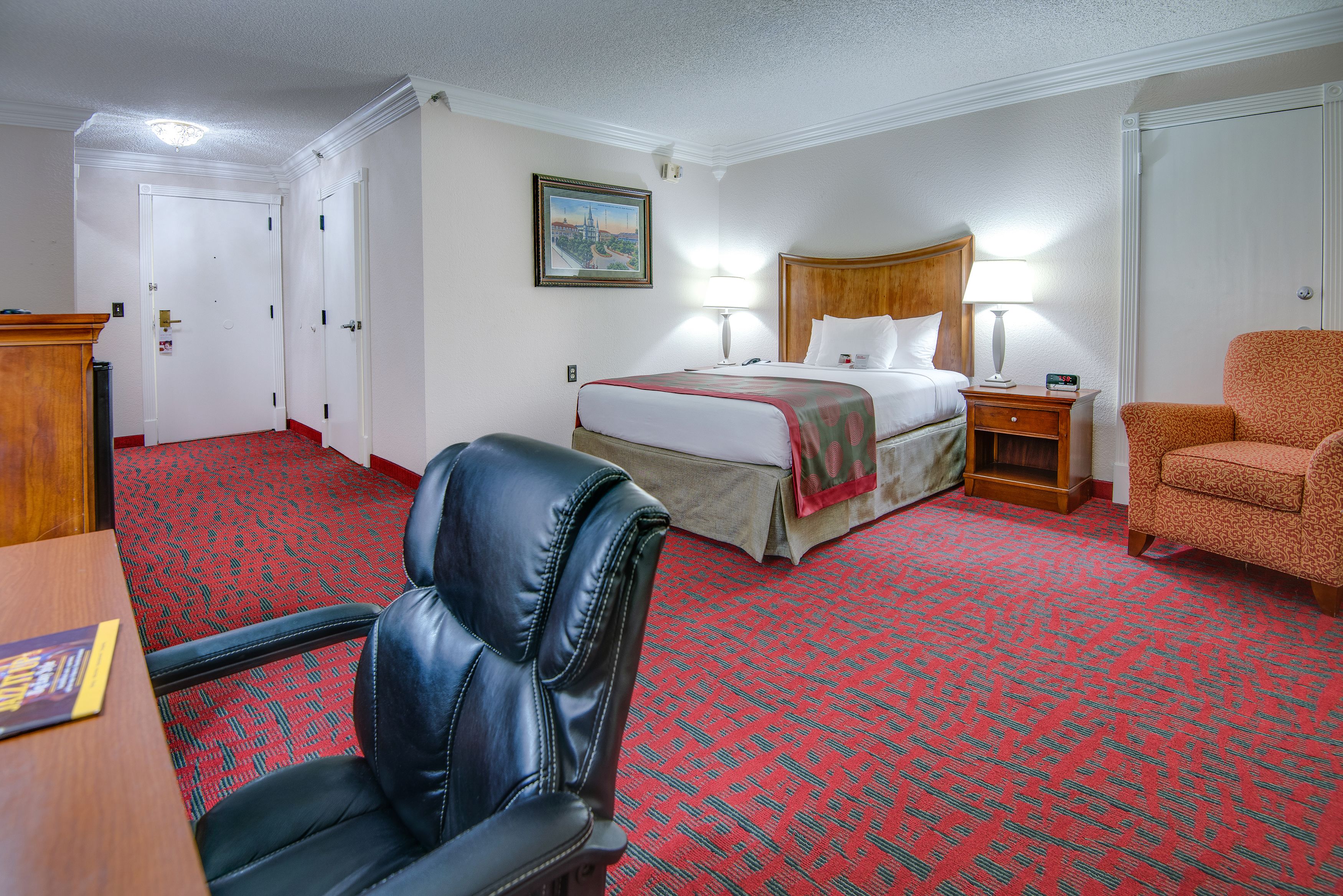 Una camera d'albergo con un letto grande, una scrivania, una poltrona in pelle e un tappeto rosso con motivo.