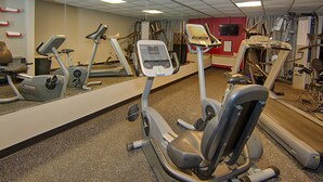 A gym with various exercise machines, a large mirror, and a television on the wall.