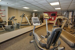 Ein Fitnessstudio mit verschiedenen Trainingsgeräten, einem großen Spiegel und einem Fernseher an der Wand.