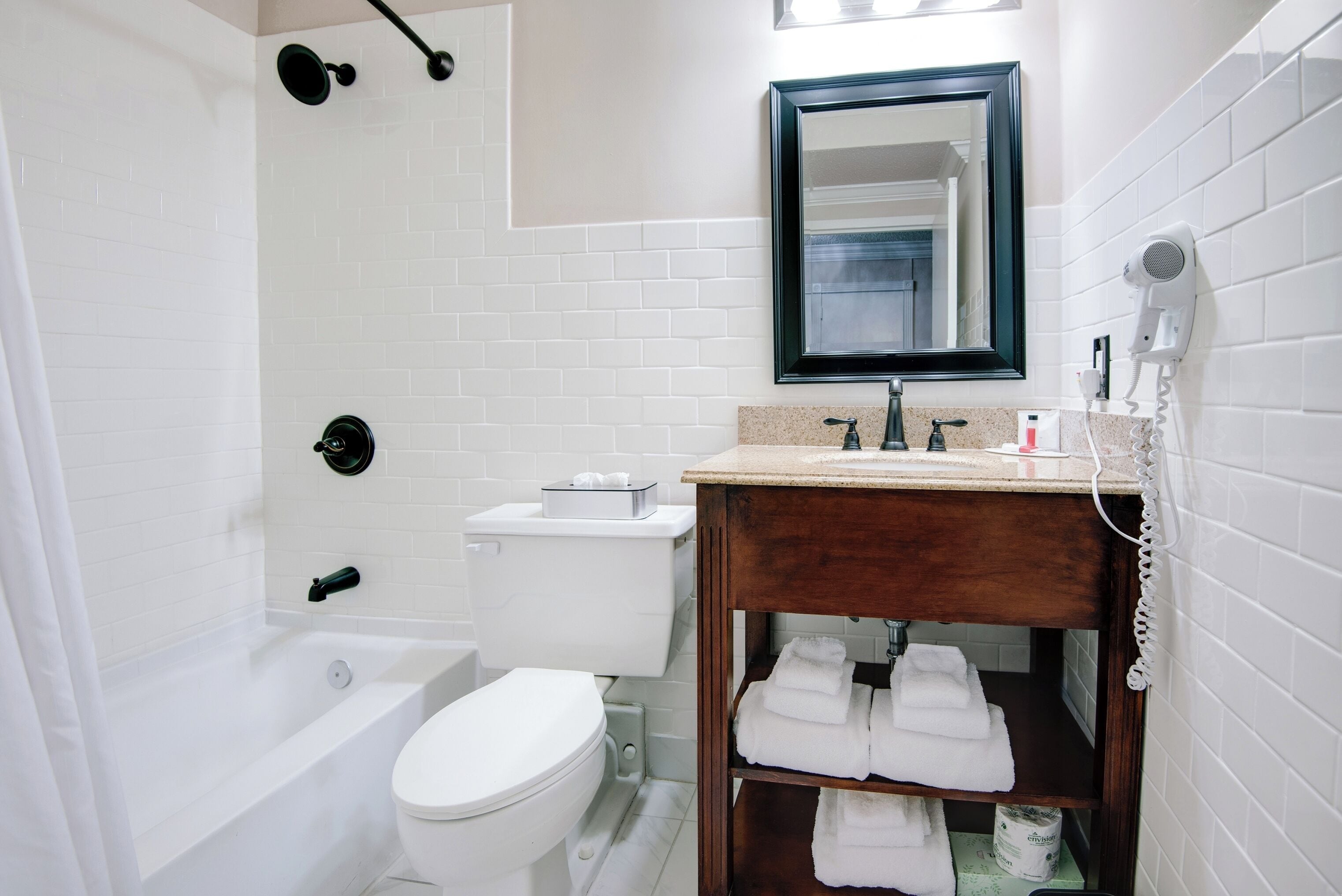 Un baño con inodoro blanco, tocador de madera con espejo, zona de ducha y un perchero para toallas.