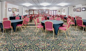 A conference room with round tables and red chairs, carpeted floor, and framed pictures on the walls. - Clarion Hotel & Suites (Metairie)