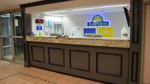 Un comptoir d’accueil dans un hôtel Days Inn, avec une horloge numérique, un ordinateur et un flacon de gel hydroalcoolique.