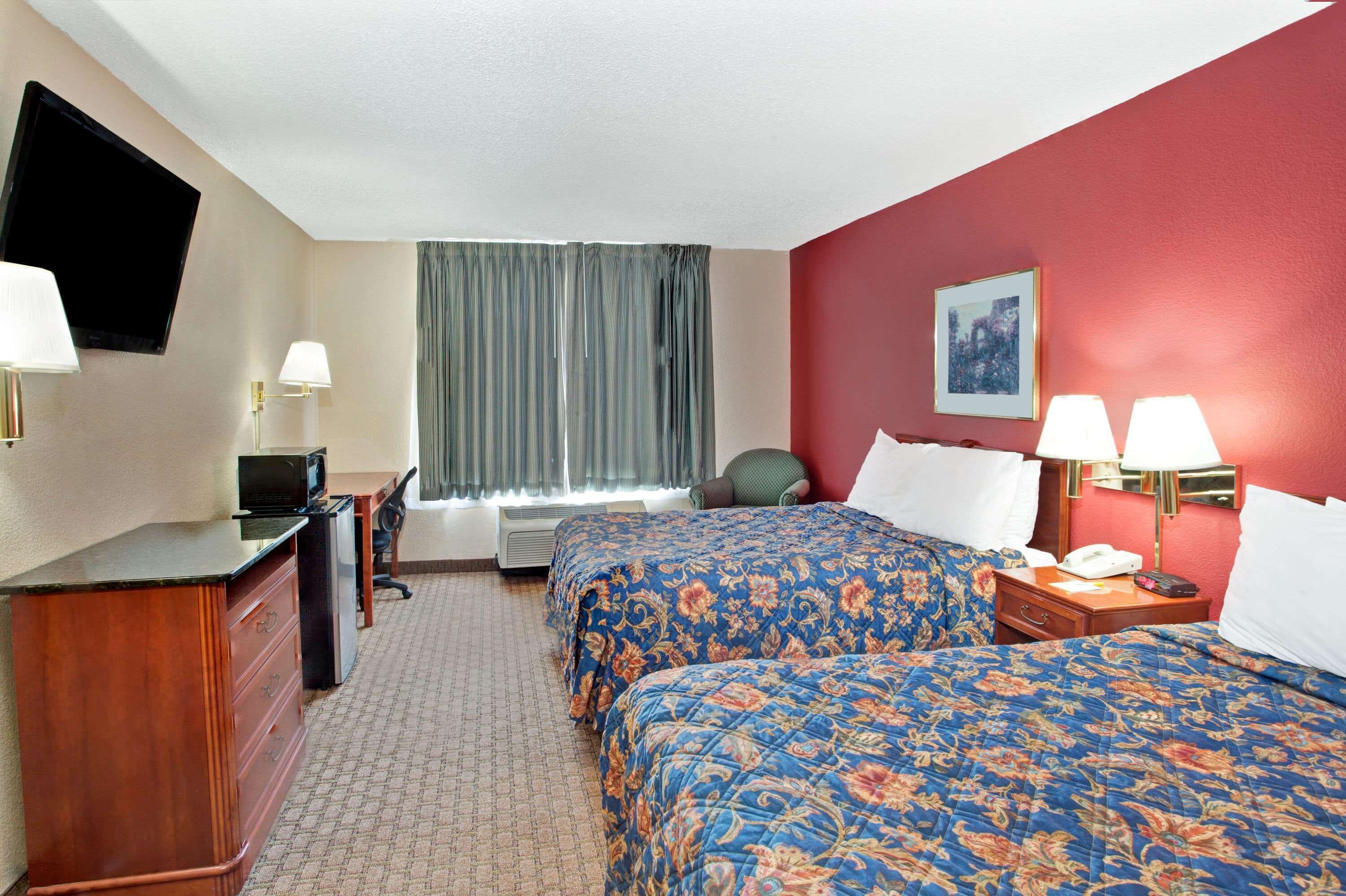 A hotel room with two beds, a desk, a TV, and a window with curtains.