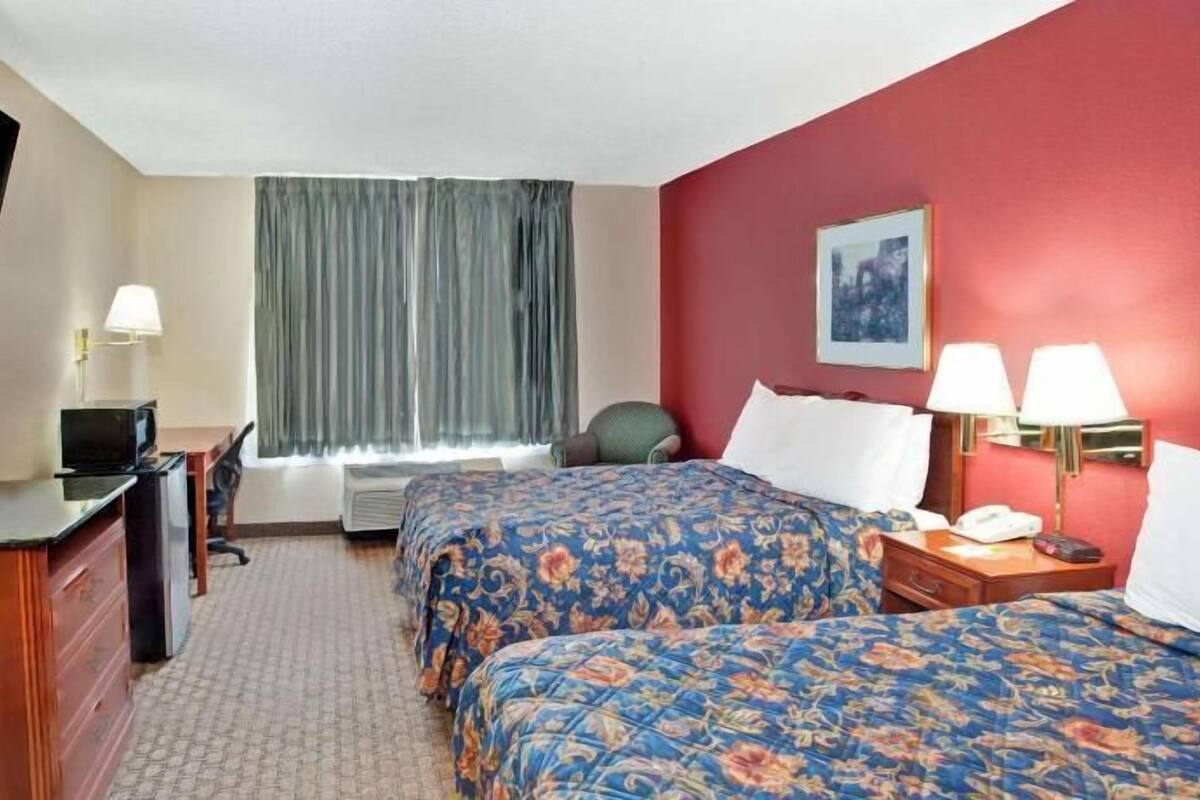 Une chambre d’hôtel avec deux lits, un bureau, une télévision et une fenêtre avec des rideaux.