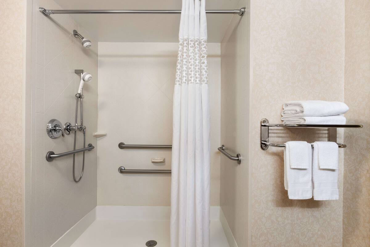 A shower with a glass door, grab bars, and a towel rack with folded towels.
