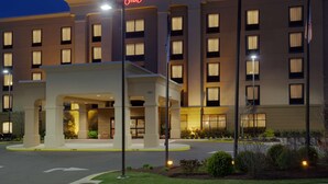 Un hotel Hampton Inn con una entrada bien iluminada, varios pisos y un asta de banderas.