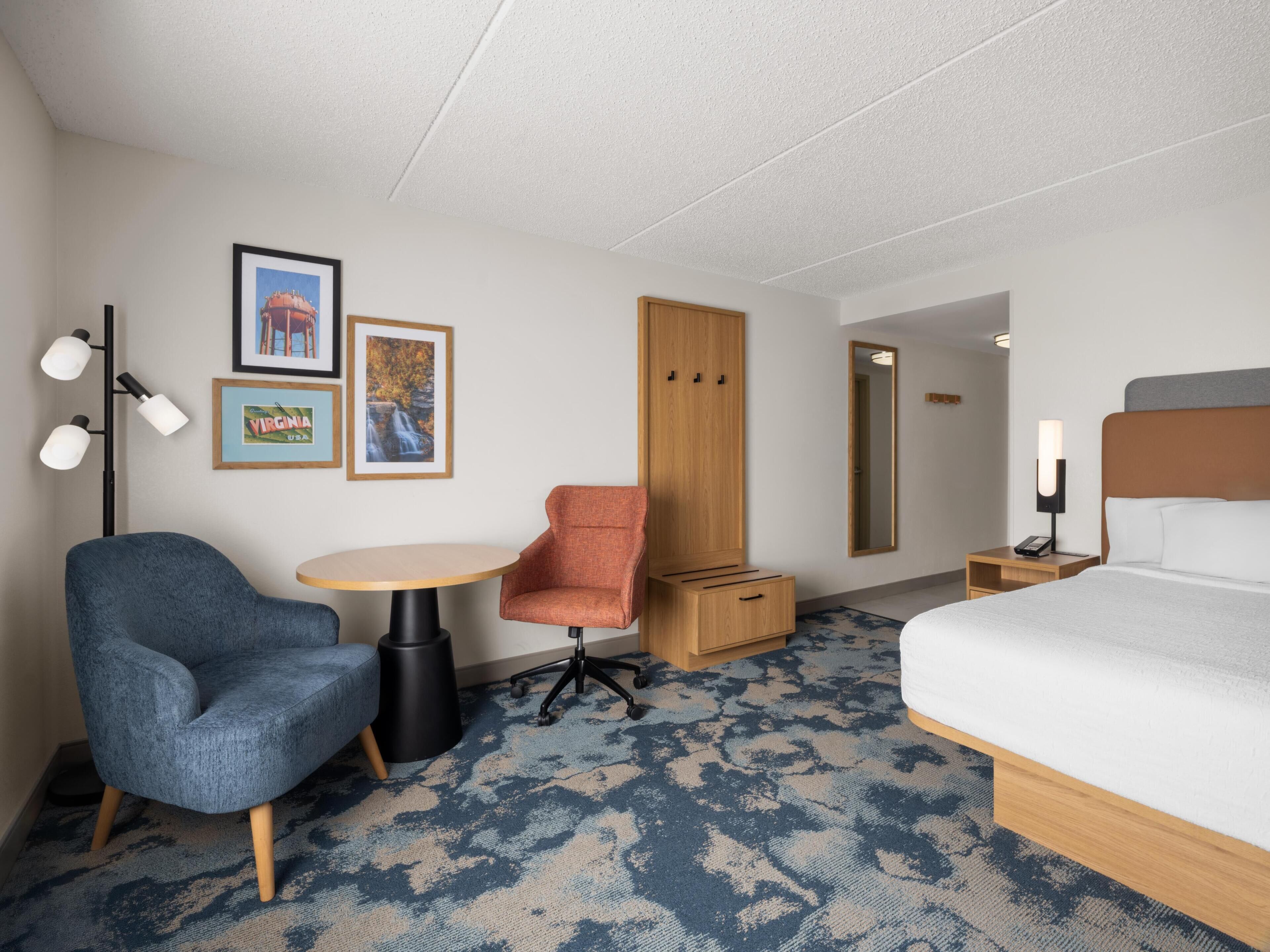A hotel room with a bed, a desk, a chair, a wardrobe, and framed pictures on the wall.