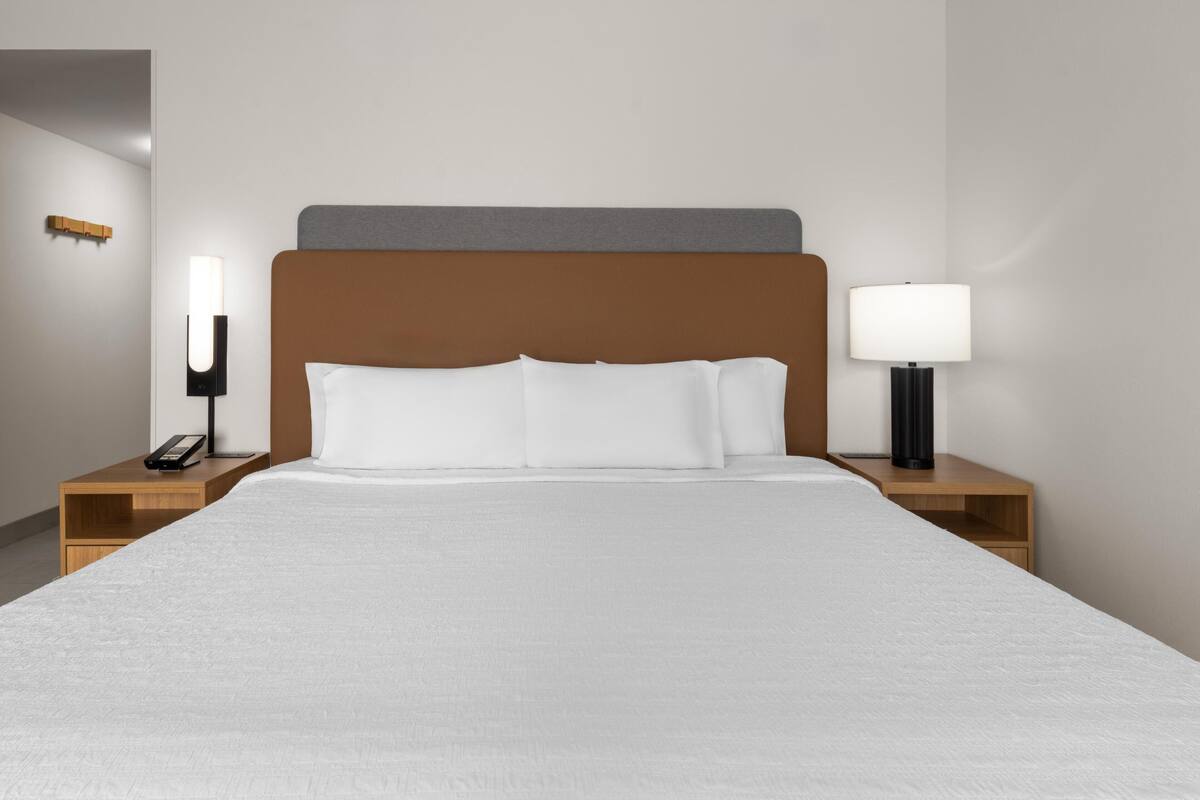 A hotel room with a bed, two bedside tables, a lamp on each table, and a wall-mounted light fixture.