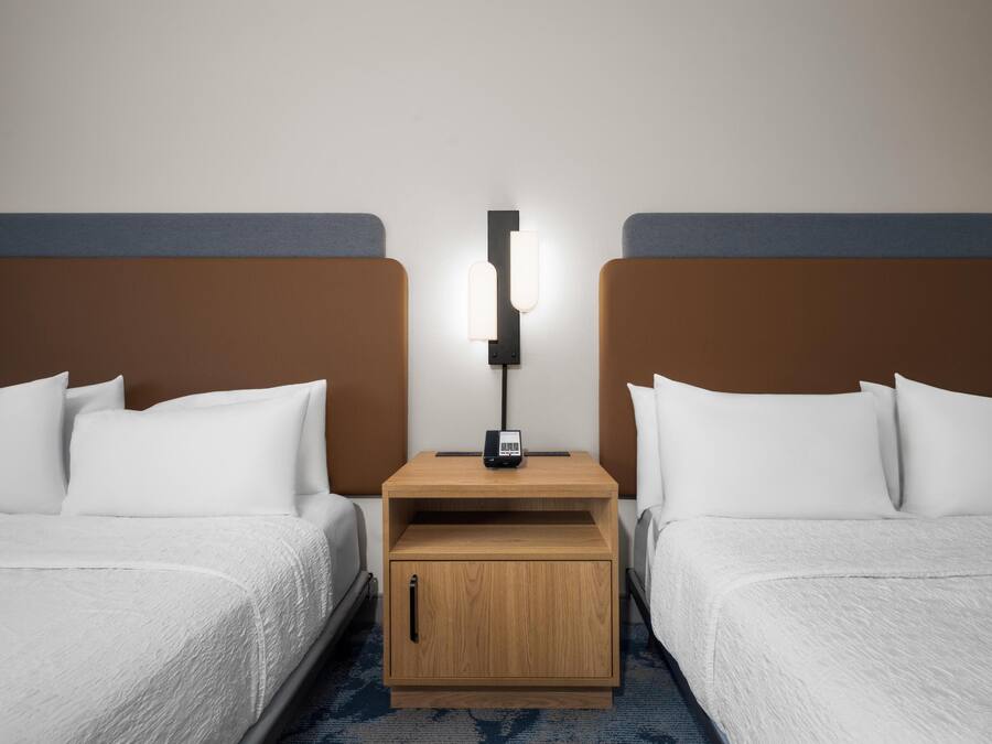 Una habitación de hotel con dos camas individuales, una mesita de noche con lámpara y un armario de madera.