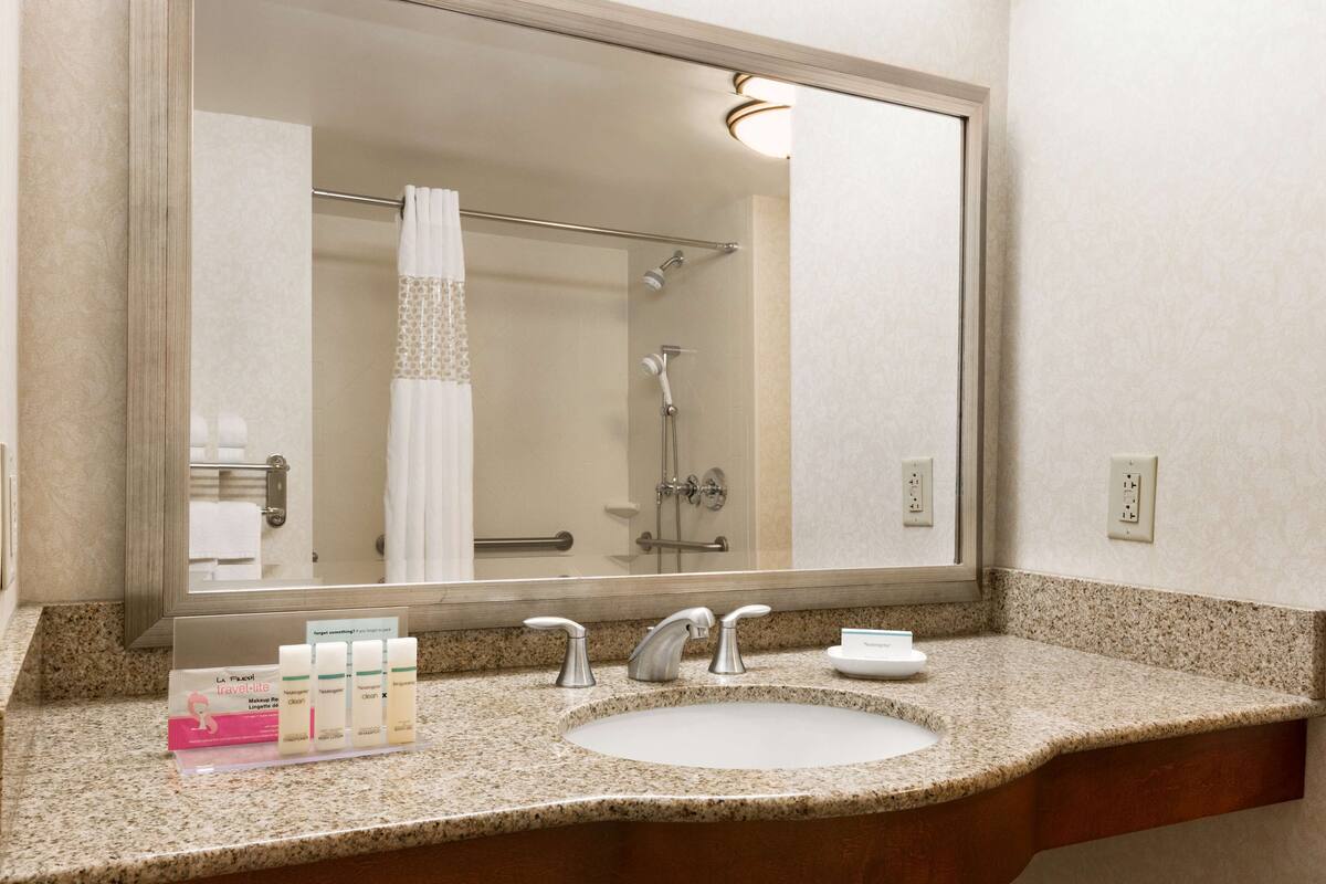A bathroom with a large mirror, a sink, and a shower.
