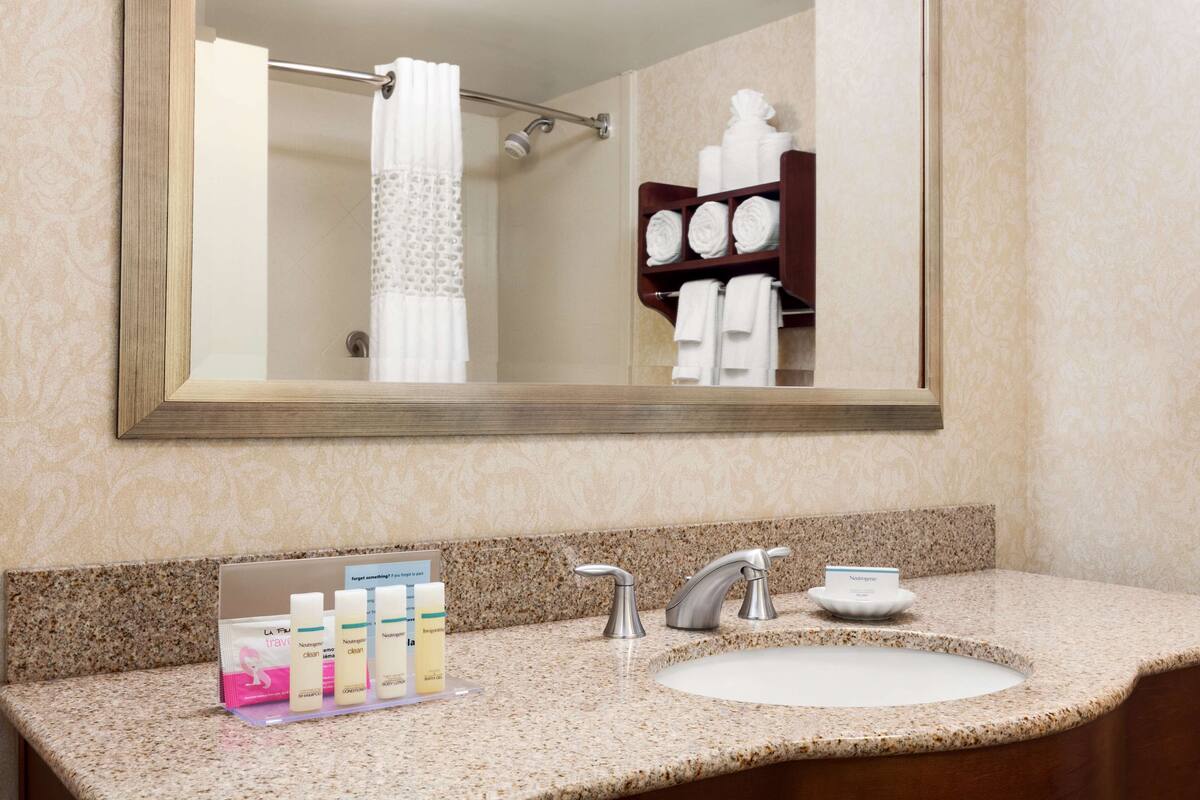 A bathroom with a large mirror, a sink with a granite countertop, and a towel rack with neatly folded towels.