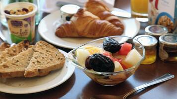 A breakfast setting with croissants, fruit, yogurt, and bread on a table.