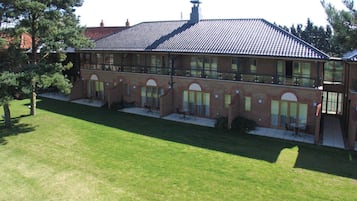 A two-story building with a tiled roof, brick walls, and multiple windows. There is a covered outdoor area with tables and chairs.