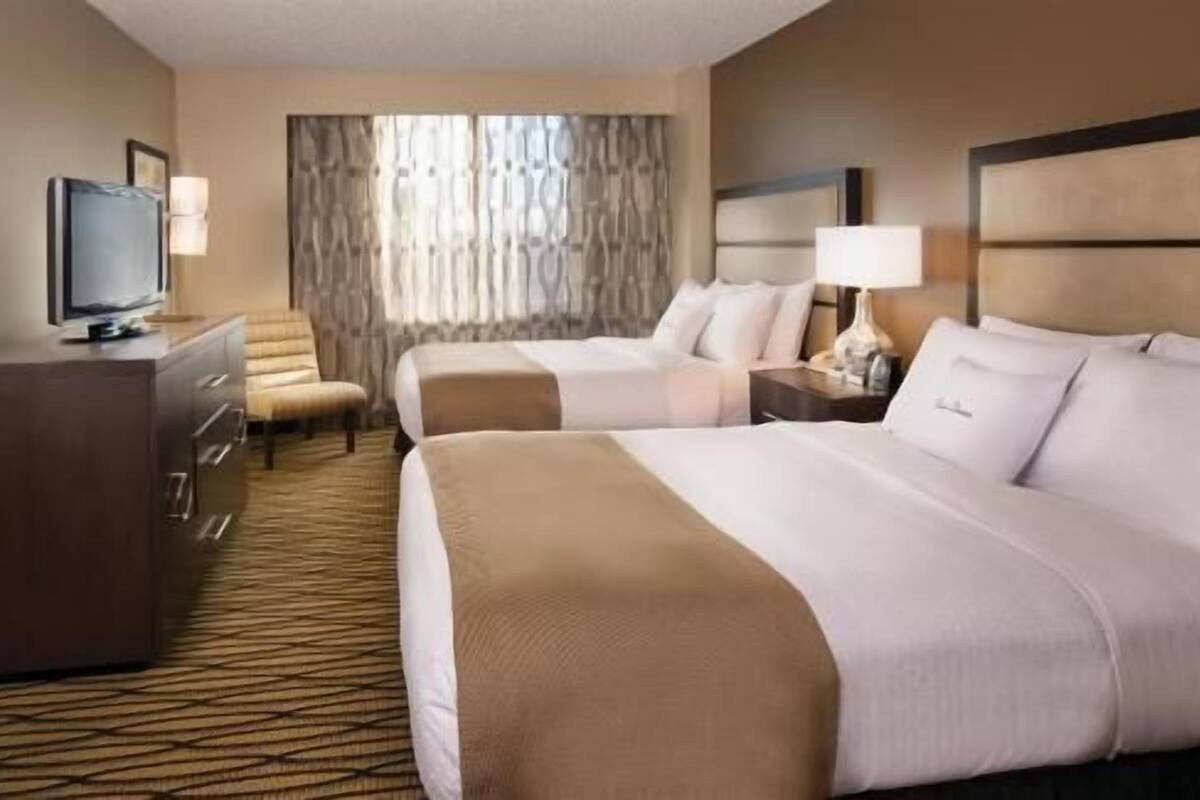 A hotel room with two beds, a television, a desk, and a window with curtains.