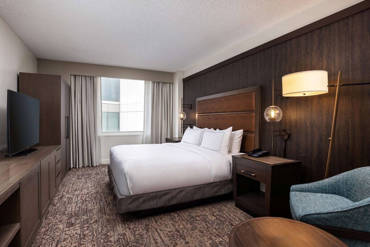 A hotel room with a large bed, a TV, a desk, and a chair.