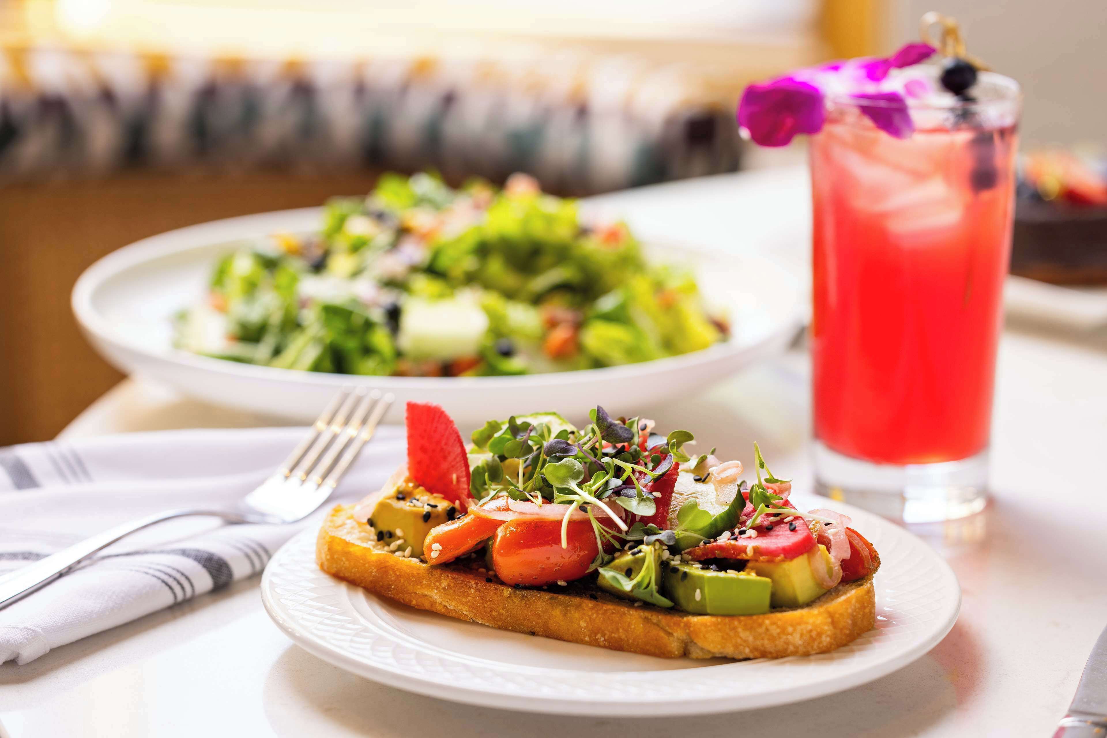 A plate of toast topped with vegetables and a glass of red drink.