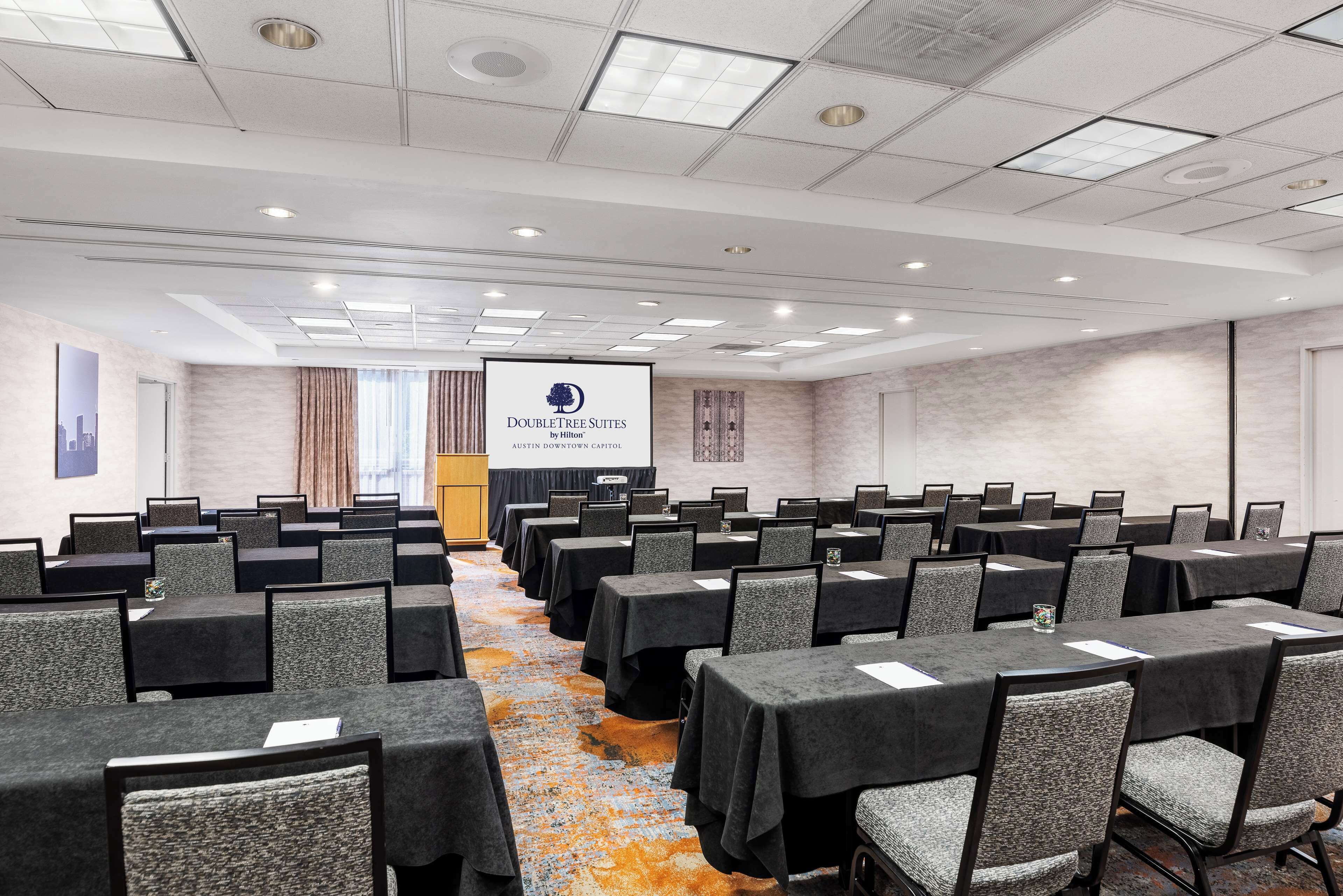 A conference room with rows of tables and chairs, a podium, and a banner reading "DoubleTree Suites by Hilton Austin Capitol".