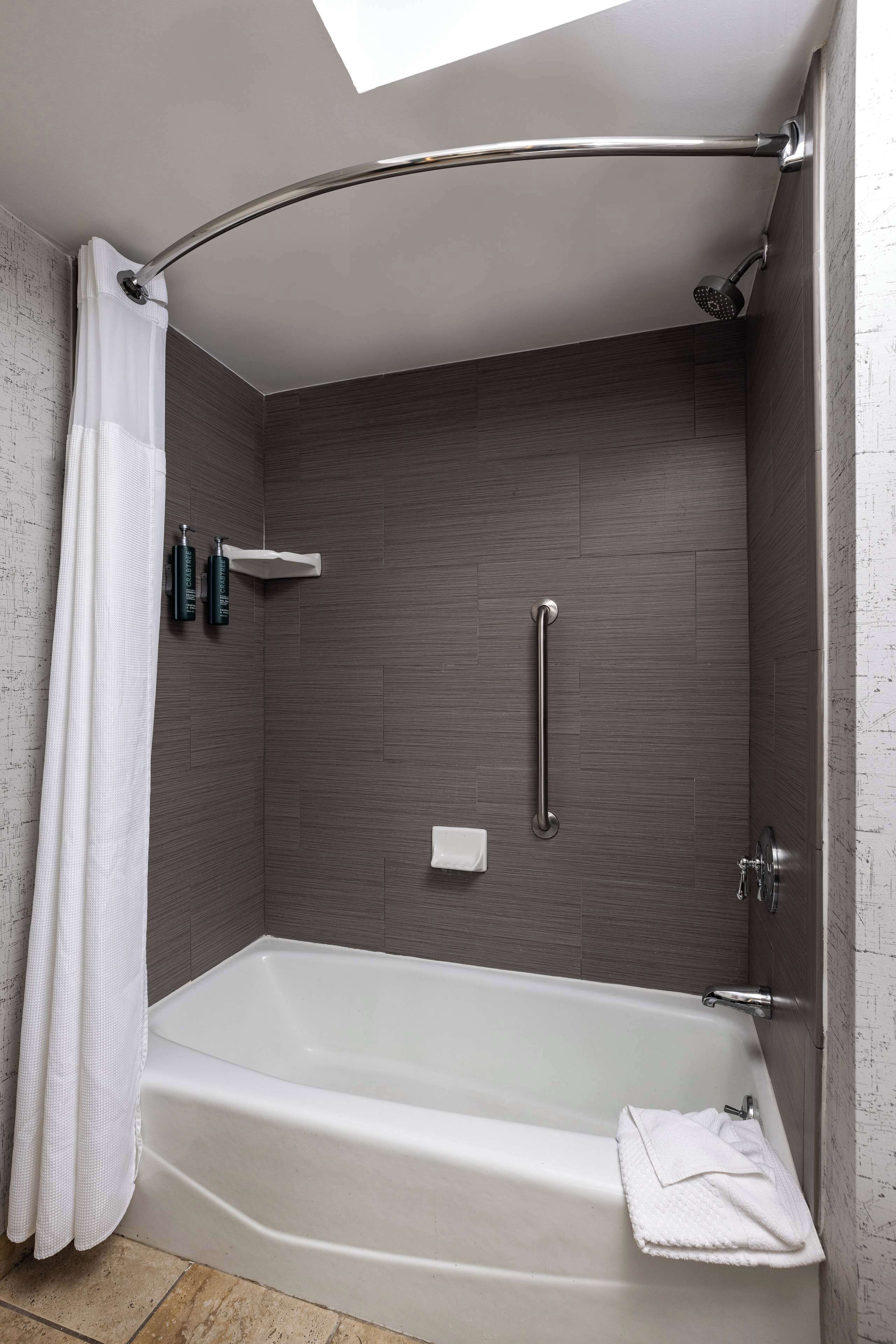 A modern bathroom with a walk-in shower, a grab bar, and a white bathtub.