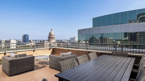 A rooftop terrace with wicker furniture, a round table, and a view of a cityscape including a dome building. - DoubleTree Suites by Hilton Austin Downtown Capitol (Austin)