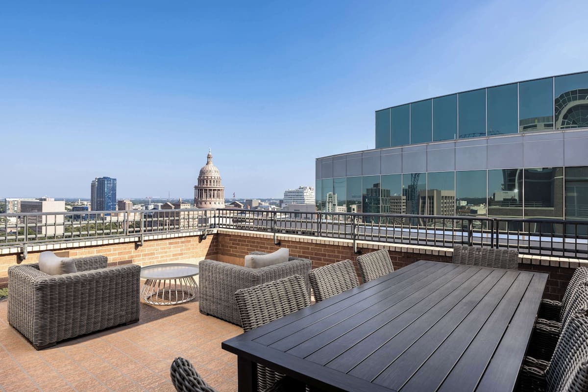 A rooftop terrace with wicker furniture, a round table, and a view of a cityscape including a dome building.