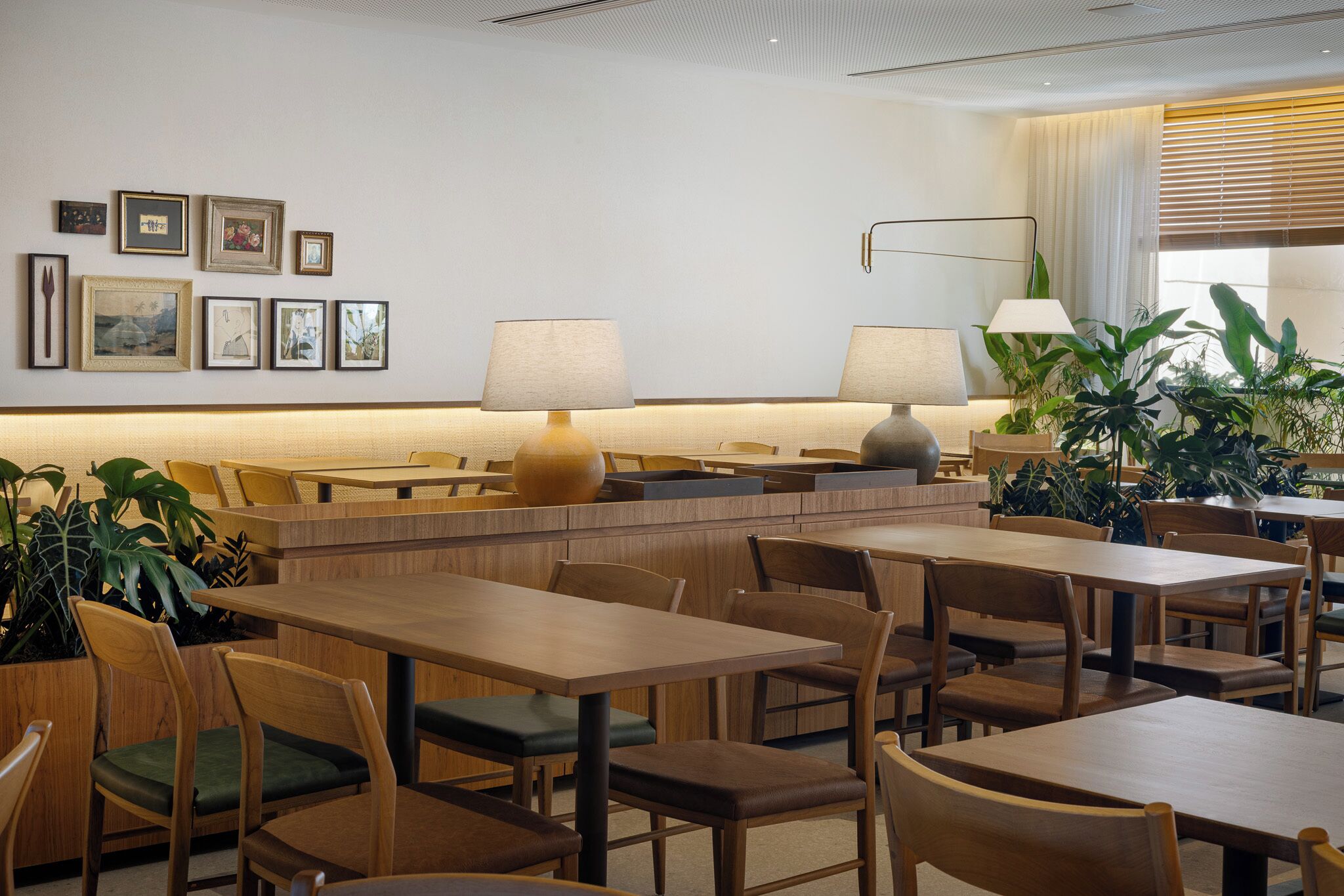 A restaurant with wooden tables and chairs, framed pictures on the wall, and potted plants.