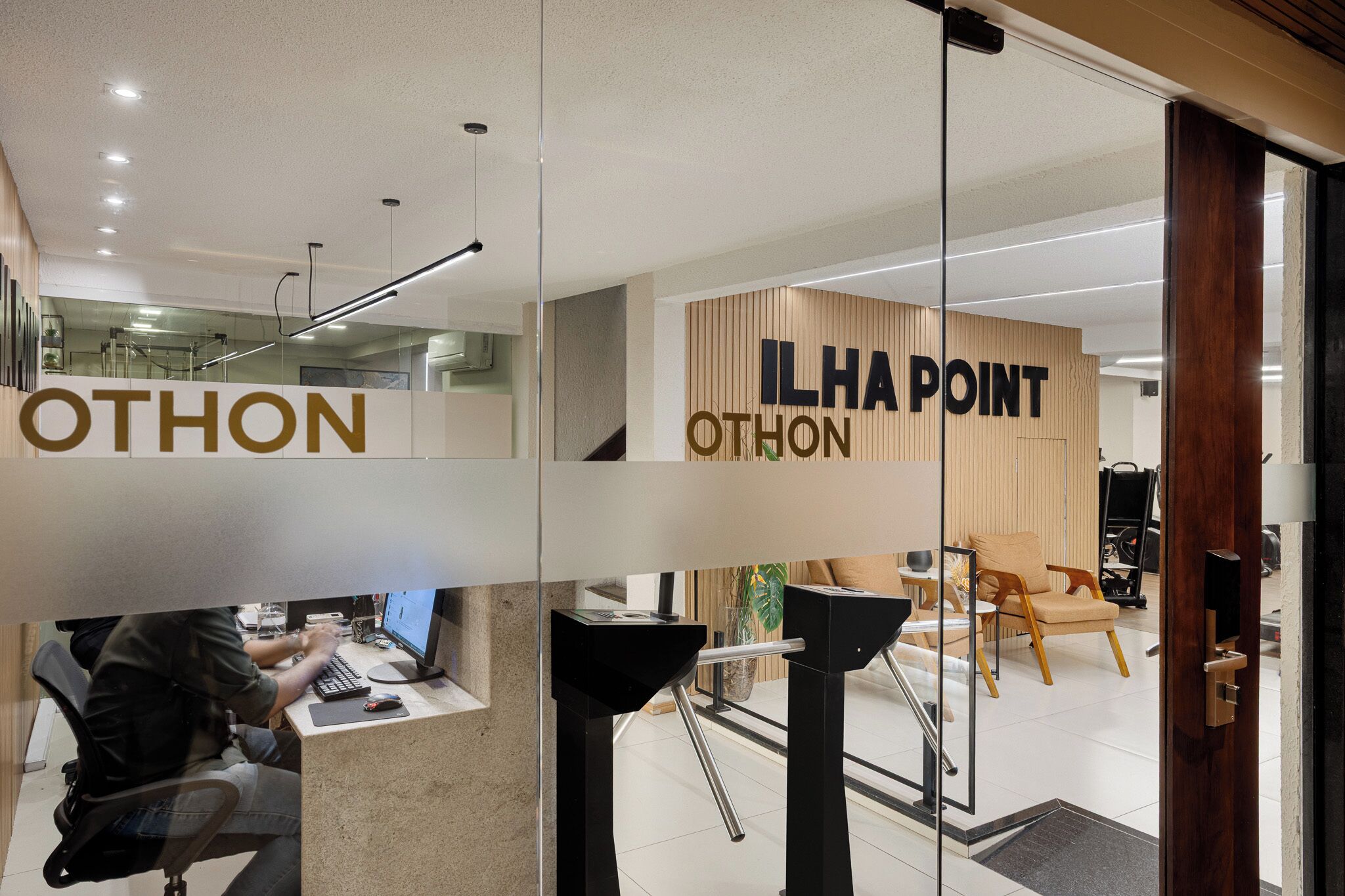 Un intérieur moderne comprenant un comptoir d’accueil, un poste informatique et un mur en bois sur lequel est inscrit le texte « ILHA POINT OTHON ».
