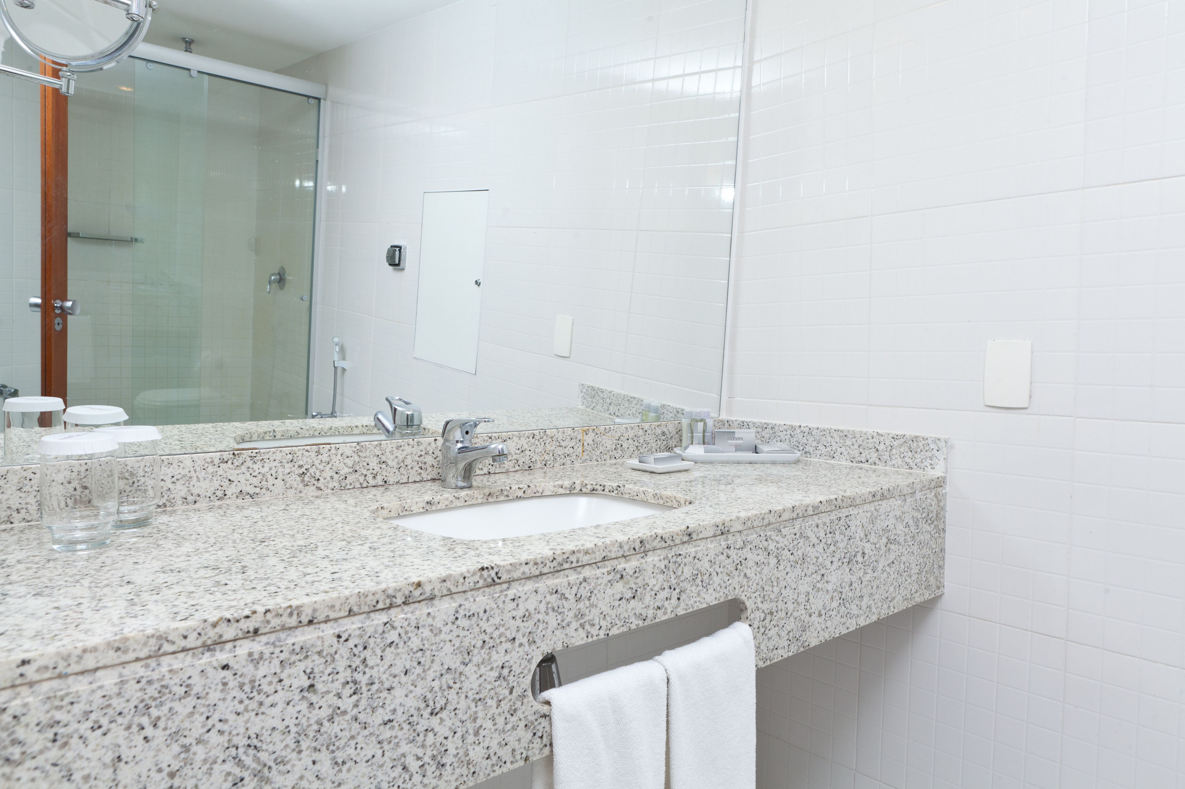 A modern bathroom with a granite countertop, two sinks, a glass shower enclosure, and a large mirror.